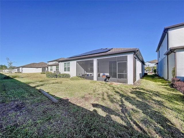 rear view of property with a lawn, a sunroom, and solar panels