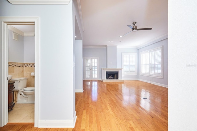 unfurnished living room with ceiling fan, light hardwood / wood-style floors, ornamental molding, and french doors