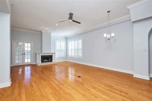 unfurnished living room featuring ceiling fan with notable chandelier, light wood-type flooring, ornamental molding, and french doors