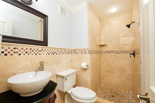 bathroom with sink, toilet, ornamental molding, tile walls, and a tile shower