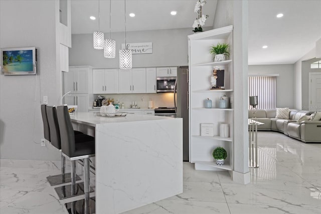 kitchen featuring pendant lighting, backsplash, white cabinets, a kitchen bar, and stainless steel appliances