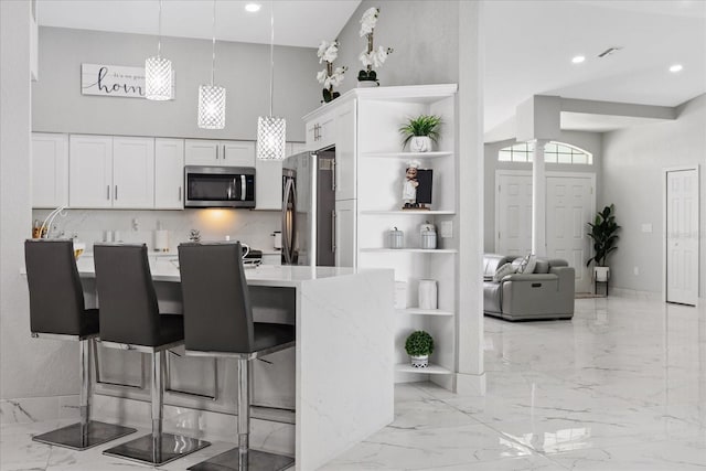 kitchen with pendant lighting, light stone counters, appliances with stainless steel finishes, a kitchen bar, and white cabinetry