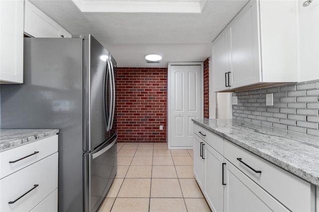 kitchen with white cabinets, stainless steel refrigerator, and brick wall