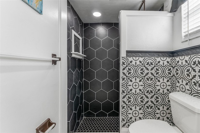 bathroom with tiled shower, toilet, and tile walls