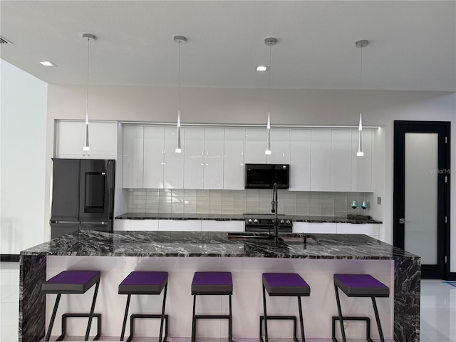 kitchen with white cabinetry, dark stone counters, hanging light fixtures, and tasteful backsplash