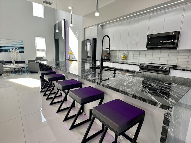 kitchen with dark stone countertops, stainless steel appliances, white cabinetry, and a kitchen bar