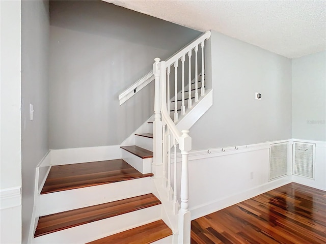 stairway with wood-type flooring and a textured ceiling