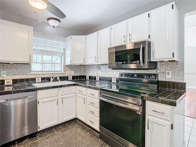 kitchen featuring tile countertops, dark tile patterned flooring, sink, appliances with stainless steel finishes, and white cabinetry