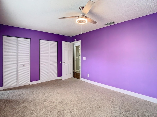 unfurnished bedroom featuring ceiling fan, carpet floors, a textured ceiling, and multiple closets