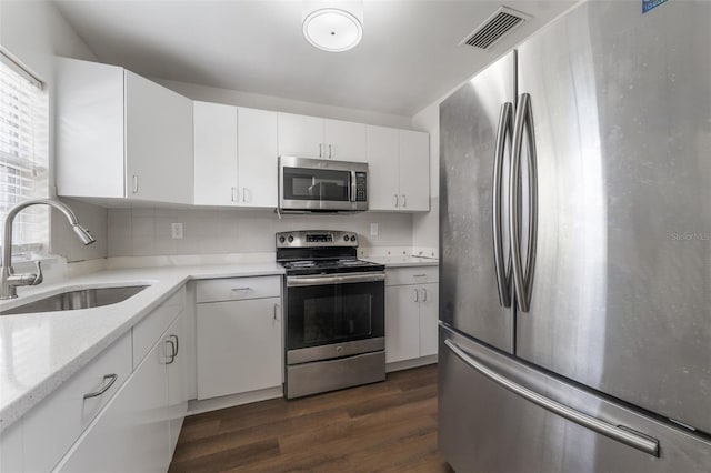 kitchen with sink, light stone countertops, appliances with stainless steel finishes, dark hardwood / wood-style flooring, and white cabinetry