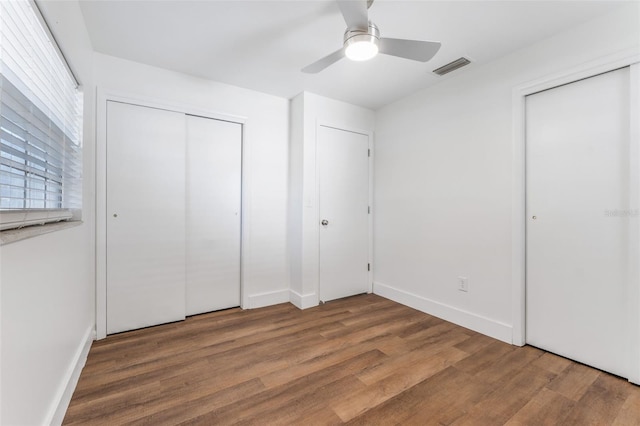 unfurnished bedroom featuring multiple closets, ceiling fan, and wood-type flooring