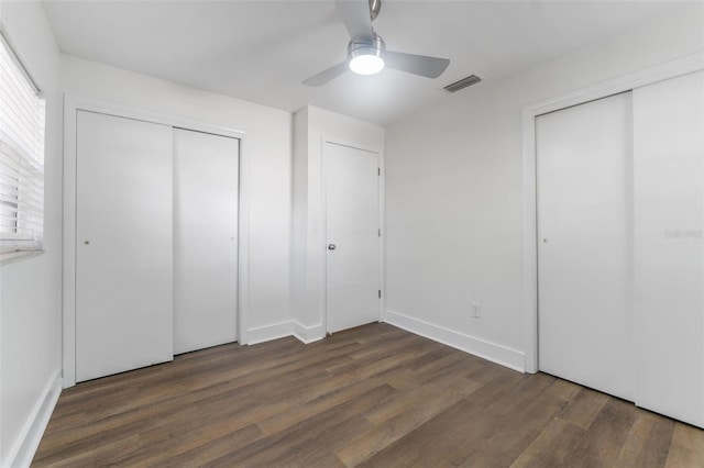 unfurnished bedroom featuring ceiling fan, dark hardwood / wood-style flooring, and two closets