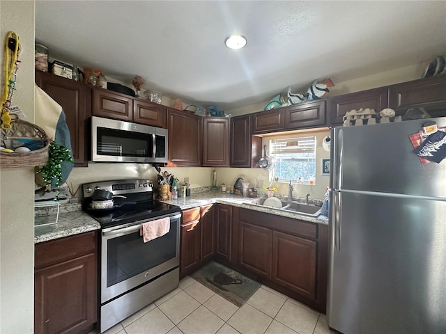 kitchen featuring dark brown cabinetry, light stone countertops, sink, light tile patterned floors, and appliances with stainless steel finishes