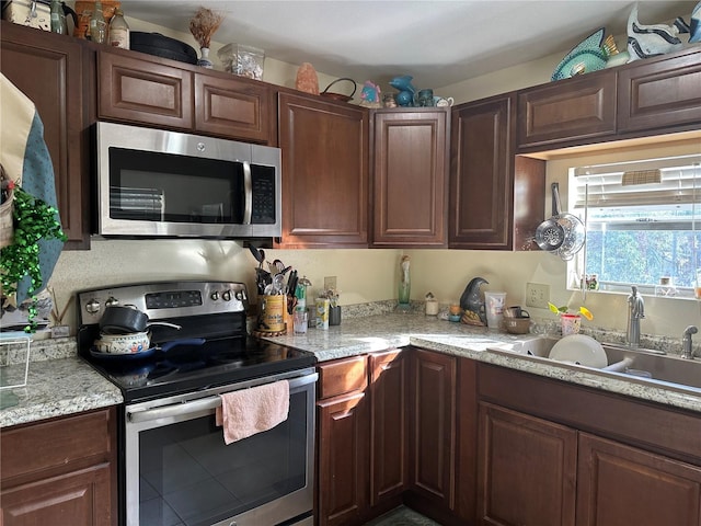 kitchen featuring light stone countertops, appliances with stainless steel finishes, dark brown cabinetry, and sink