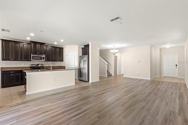 kitchen featuring appliances with stainless steel finishes, dark brown cabinetry, a center island with sink, and light hardwood / wood-style flooring