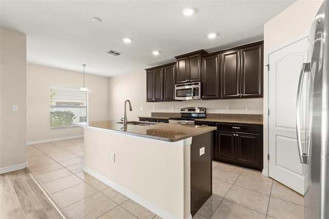 kitchen featuring sink, light tile patterned floors, stainless steel appliances, and an island with sink