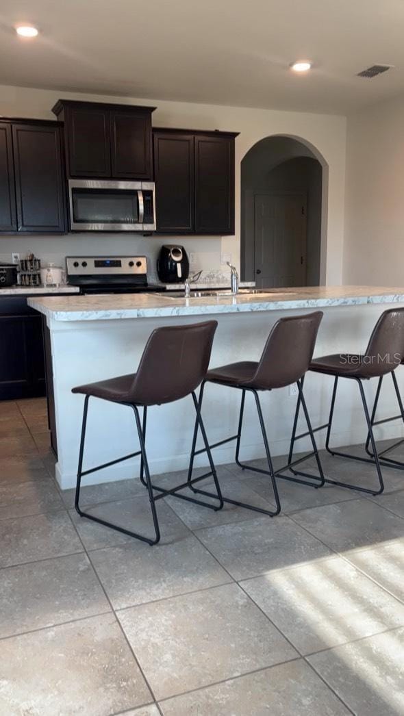 kitchen with a kitchen breakfast bar, dark brown cabinetry, electric range, and a kitchen island with sink