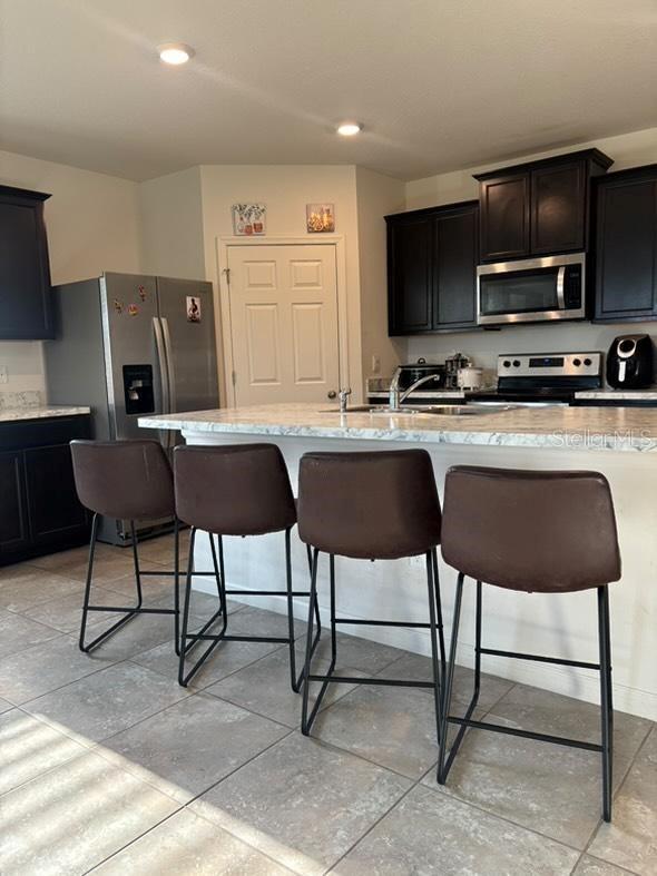 kitchen with a kitchen bar, sink, stainless steel appliances, and an island with sink