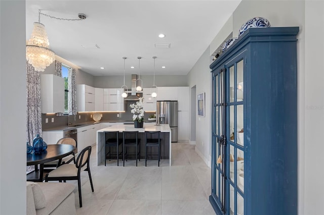 kitchen with wall chimney range hood, white cabinetry, a kitchen breakfast bar, stainless steel fridge, and a center island