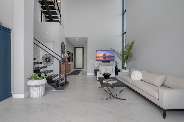 living room featuring stairway, baseboards, a high ceiling, and finished concrete floors