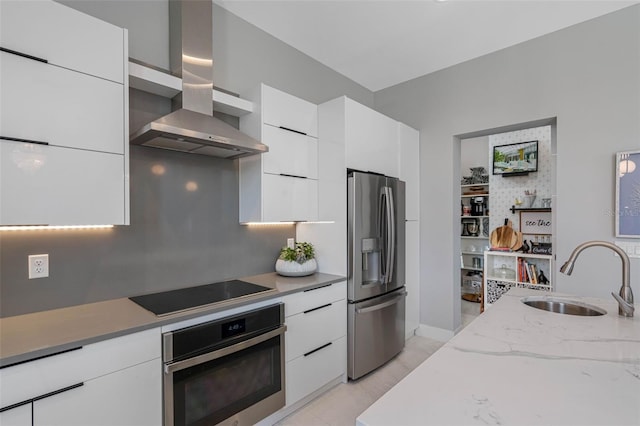 kitchen with a sink, wall chimney range hood, stainless steel appliances, white cabinetry, and modern cabinets