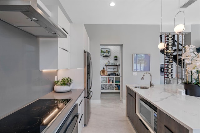 kitchen with modern cabinets, a sink, white cabinetry, appliances with stainless steel finishes, and wall chimney exhaust hood