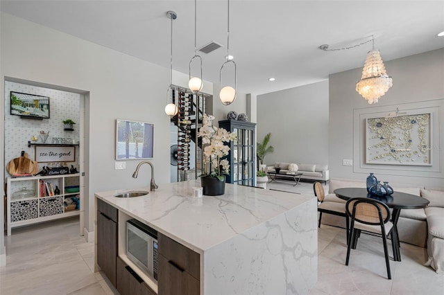 kitchen with open floor plan, a center island with sink, stainless steel microwave, and a sink