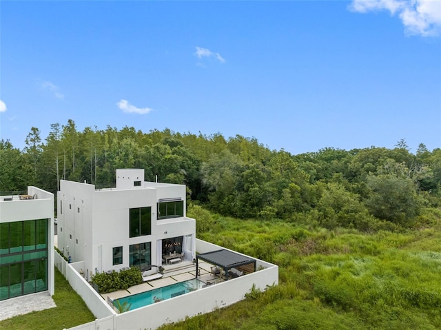 back of property featuring stucco siding, a view of trees, a patio, fence, and a fenced in pool