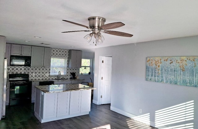 kitchen featuring sink, dark stone counters, gray cabinets, a kitchen island, and black appliances