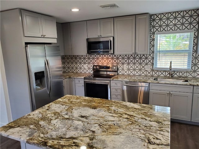 kitchen featuring gray cabinets, stainless steel appliances, dark wood-type flooring, light stone counters, and sink