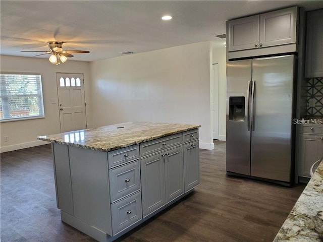 kitchen with light stone countertops, dark hardwood / wood-style floors, stainless steel fridge with ice dispenser, gray cabinets, and ceiling fan