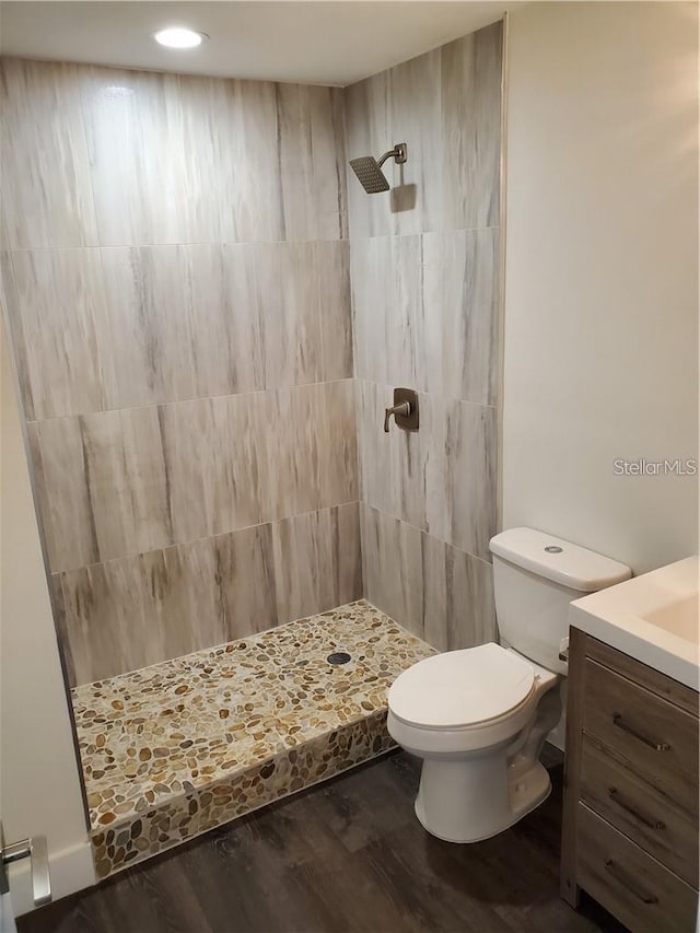 bathroom with a tile shower, wood-type flooring, vanity, and toilet