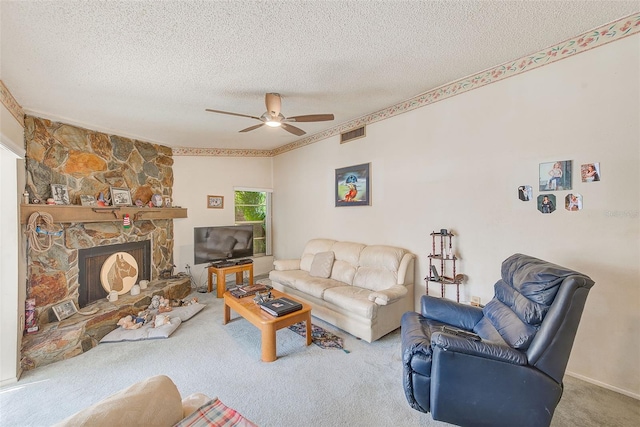 carpeted living room with a textured ceiling, a stone fireplace, and ceiling fan