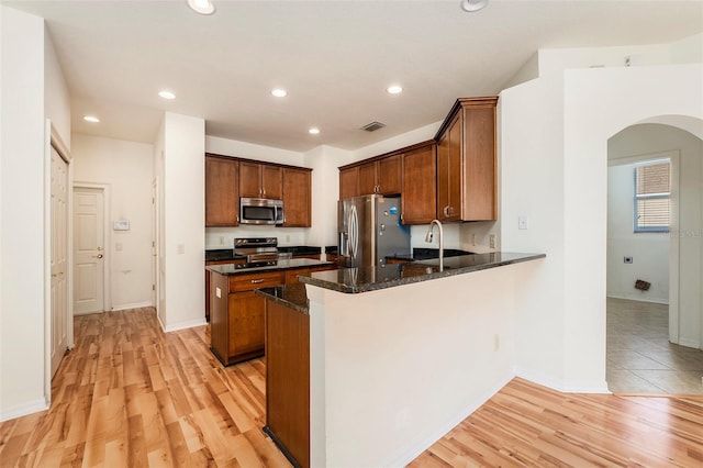 kitchen with dark stone countertops, kitchen peninsula, stainless steel appliances, and light hardwood / wood-style flooring