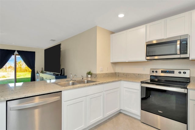 kitchen with kitchen peninsula, appliances with stainless steel finishes, light stone counters, sink, and white cabinets