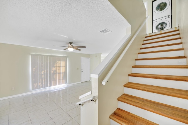 staircase with tile patterned floors, ceiling fan, a textured ceiling, and stacked washer and clothes dryer