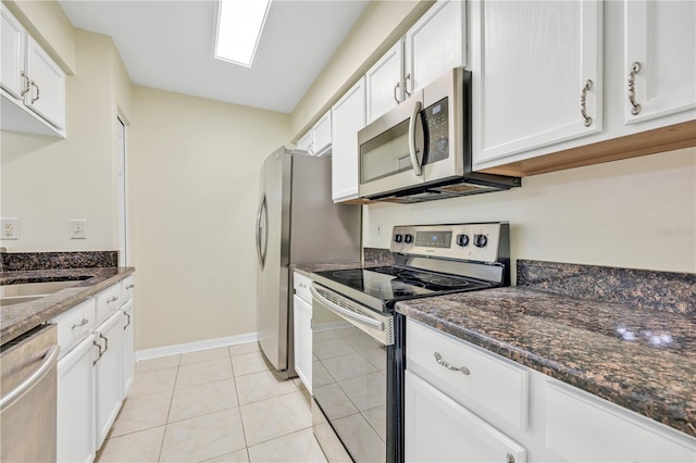 kitchen with dark stone countertops, white cabinetry, light tile patterned floors, and stainless steel appliances