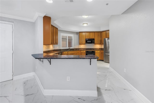 kitchen featuring kitchen peninsula, crown molding, dark stone counters, a breakfast bar, and black appliances