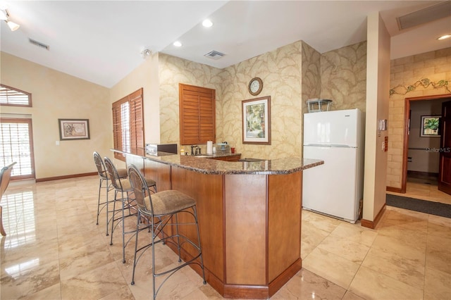 kitchen with a breakfast bar area, dark stone countertops, and white refrigerator