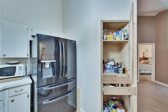 kitchen with white cabinetry, black fridge, and light tile patterned floors