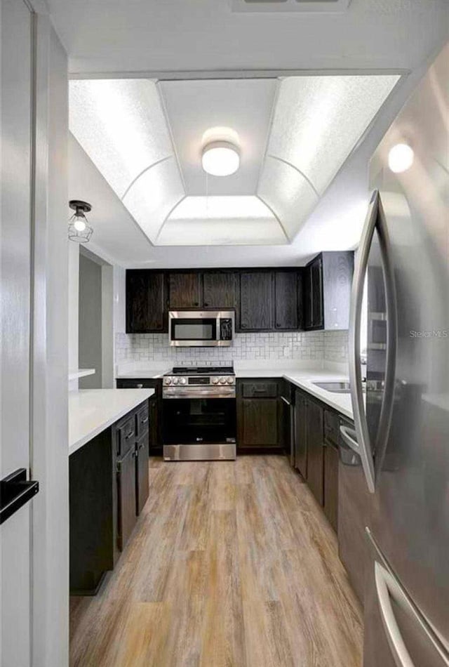 kitchen featuring backsplash, dark brown cabinets, light hardwood / wood-style floors, and stainless steel appliances