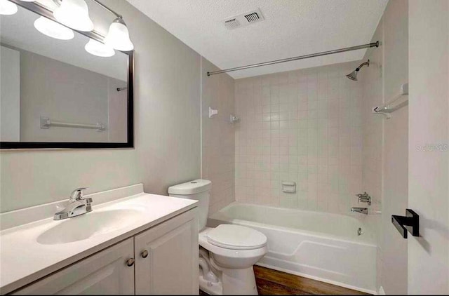 full bathroom featuring vanity, a textured ceiling, tiled shower / bath combo, wood-type flooring, and toilet