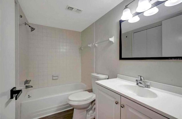 full bathroom with hardwood / wood-style floors, vanity, tiled shower / bath combo, and toilet