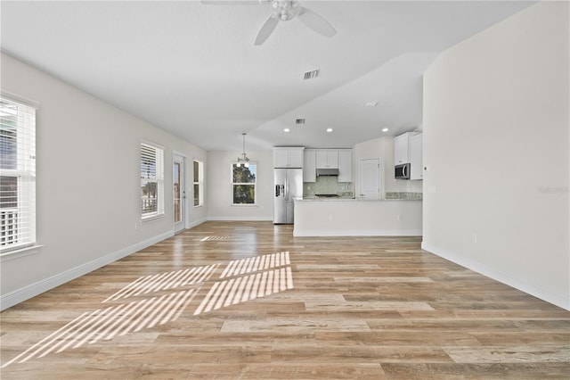 unfurnished living room with ceiling fan with notable chandelier, light hardwood / wood-style floors, and lofted ceiling