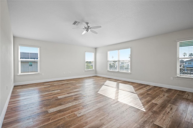 unfurnished room featuring a textured ceiling, dark hardwood / wood-style floors, ceiling fan, and a healthy amount of sunlight