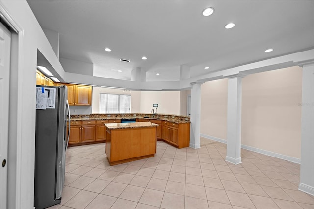 kitchen featuring a sink, a center island, freestanding refrigerator, light stone countertops, and ornate columns