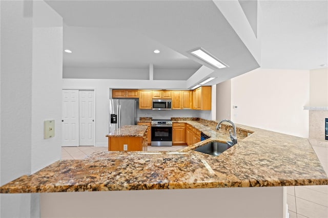 kitchen with sink, light tile patterned floors, light stone countertops, appliances with stainless steel finishes, and kitchen peninsula