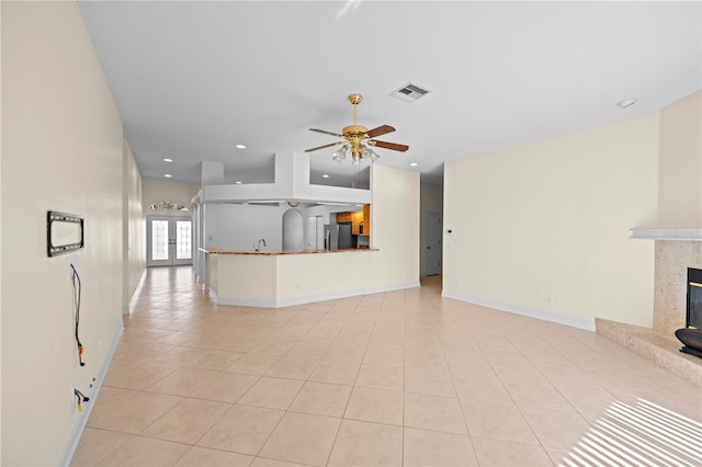 unfurnished living room with french doors, ceiling fan, sink, a tile fireplace, and light tile patterned floors