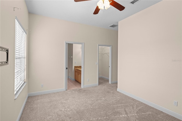 unfurnished bedroom featuring light carpet, ensuite bath, ceiling fan, a spacious closet, and a closet