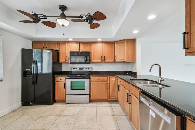 kitchen featuring light tile patterned flooring, sink, a tray ceiling, dark stone counters, and black appliances